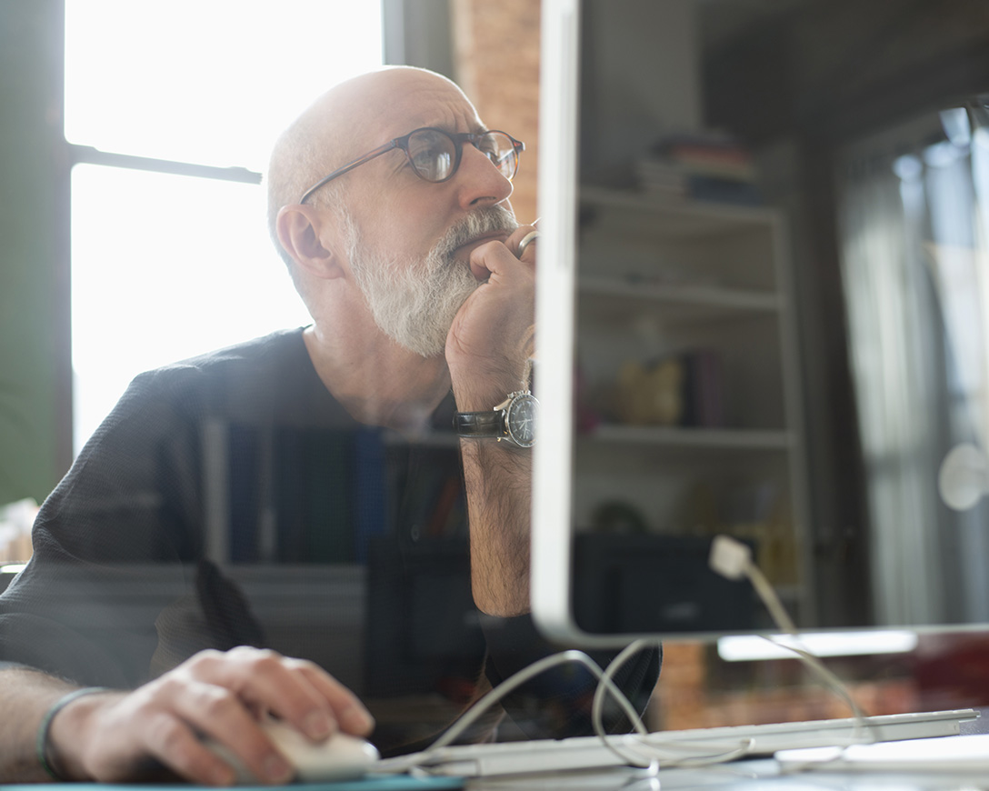 Cyber Resilience – A man rests his chin in his hand and gazes thoughtfully at his desktop monitor