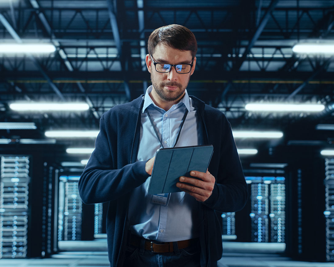 Proven Resiliency – IT Specialist works on a tablet while he walks between rows of server racks in a data center