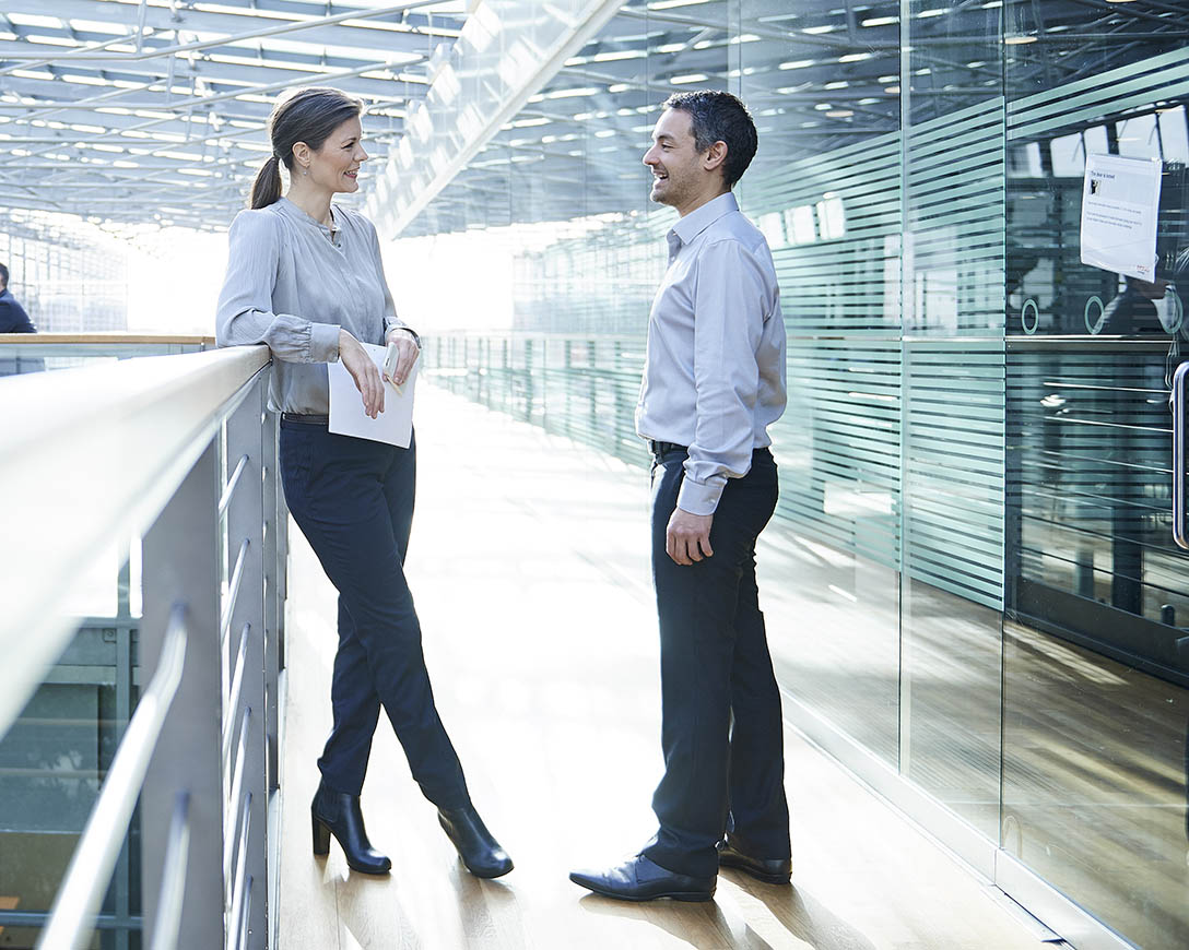 Leadership - Two C-suite colleagues have a conversation in the hallway balcony of a modern office building