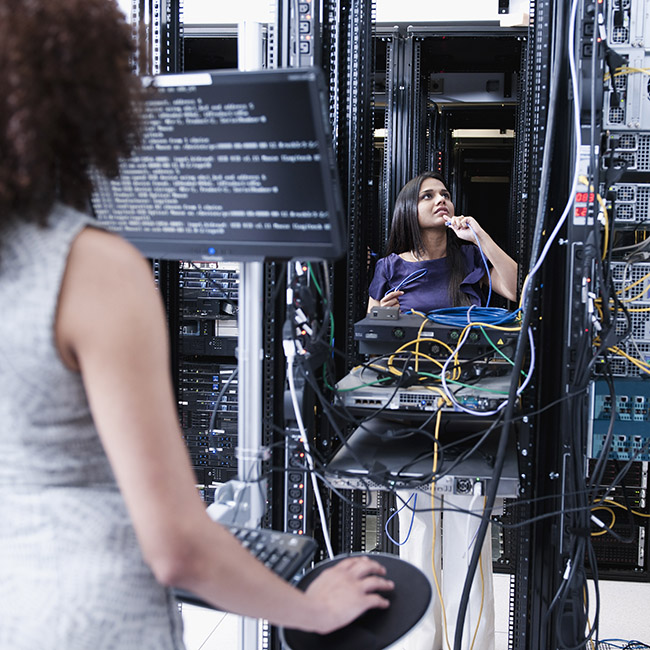 Two women in a server room, one at a terminal