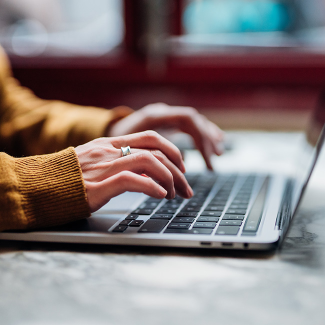 A person's hands typing with determination on a laptop