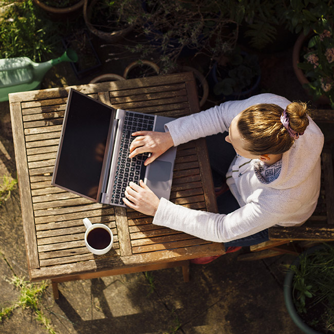 Woman working on a laptop, seated at a small, wooden patio table
