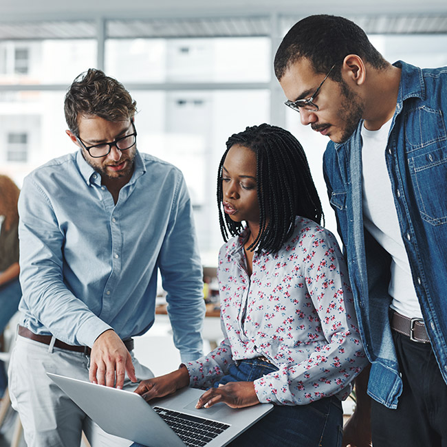 Three coworkers analyze and discuss data on a laptop