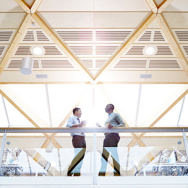 Two men standing on a balcony, facing each other and talking