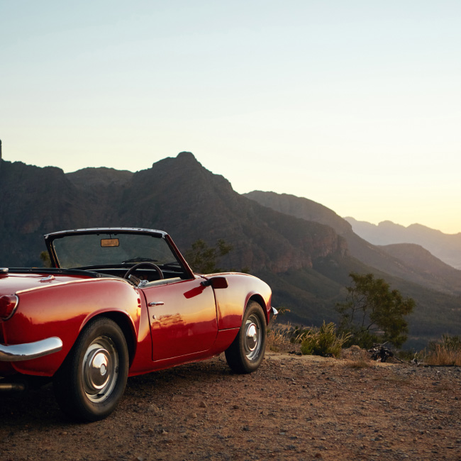 A red convertible car parked on a dirt road