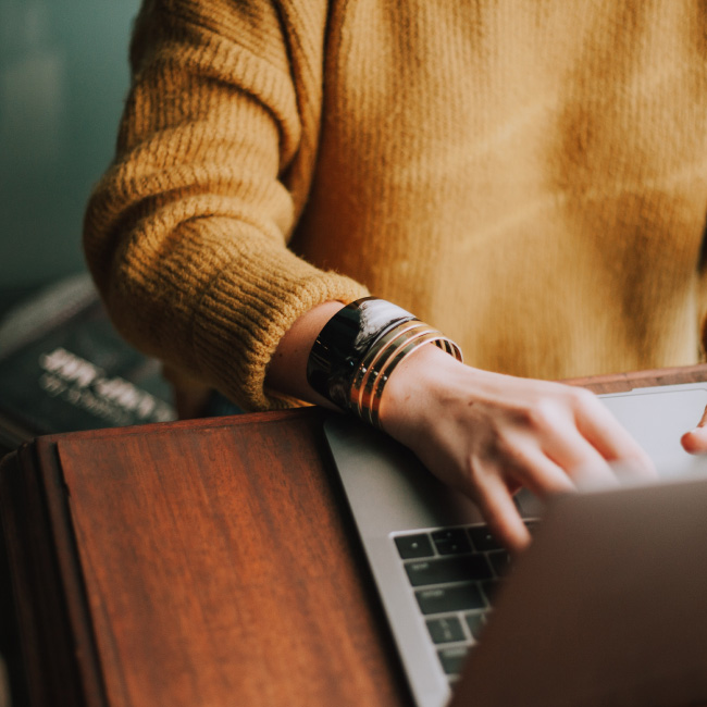 Uma mulher com um suéter amarelo é vista digitando diligentemente em um laptop
