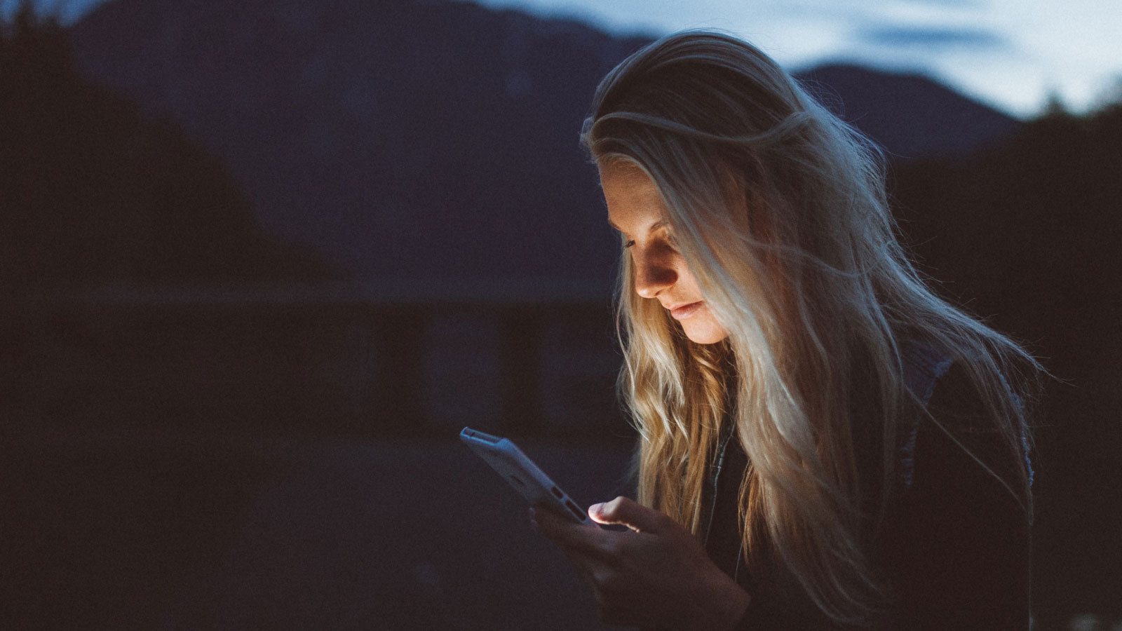 A woman engrossed in her phone's glow, captivated by its screen, amidst the darkness of the night.