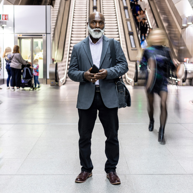 A man in a suit stands in front of an escalator, exuding an air of mystery and sophistication.