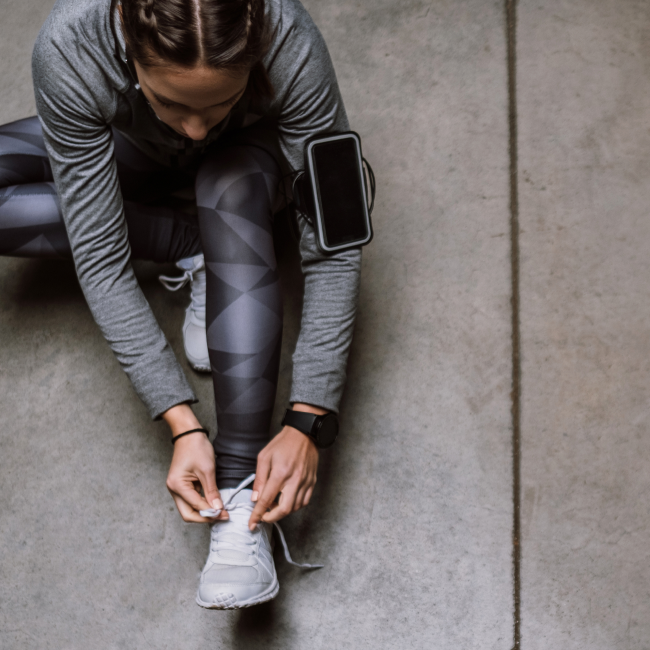 A woman tying her shoes on a concrete floor, preparing for her daily activities with focus and determination.