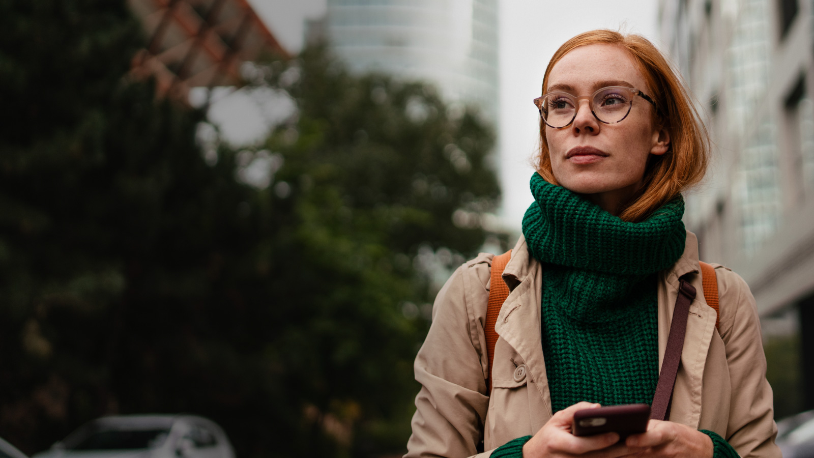 A woman wearing glasses and a green sweater is engrossed in her phone.