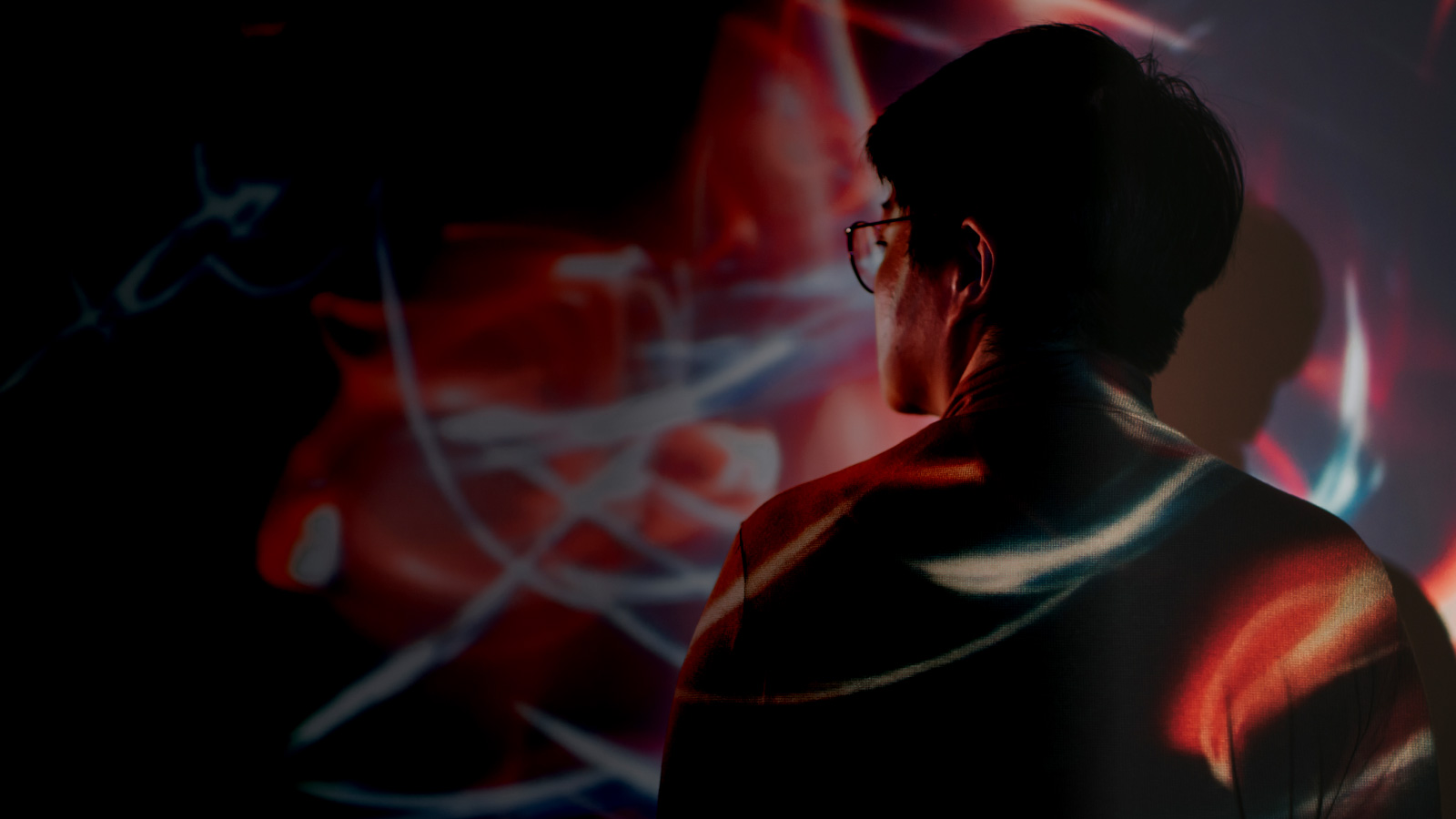 A person standing in a dimly lit room with a red light illuminating him from behind.