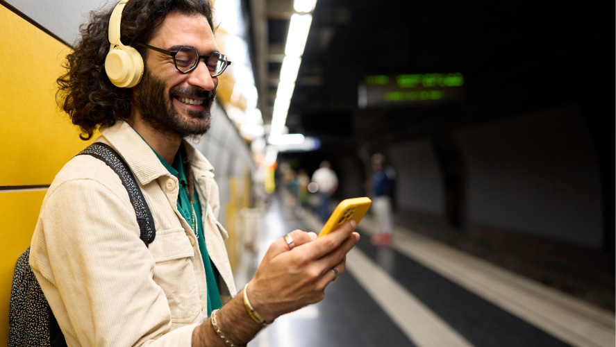 A man wearing headphones and holding a yellow phone, engrossed in audio content or communication.