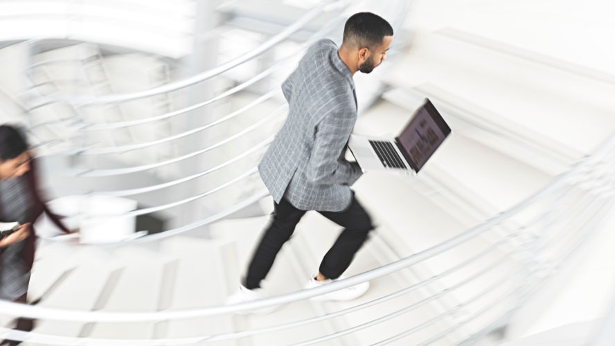 Un homme d'affaires descend les escaliers avec assurance, un ordinateur portable à la main, incarnant le professionnalisme et la productivité.