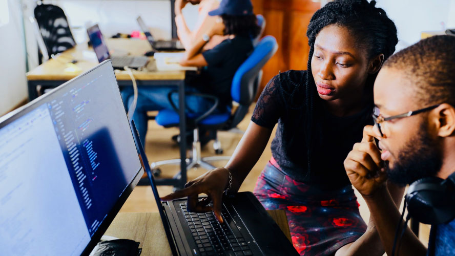 Two individuals collaborating on a computer in a professional workplace setting.