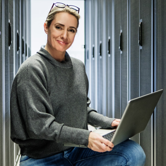 Woman working in server room with laptop.