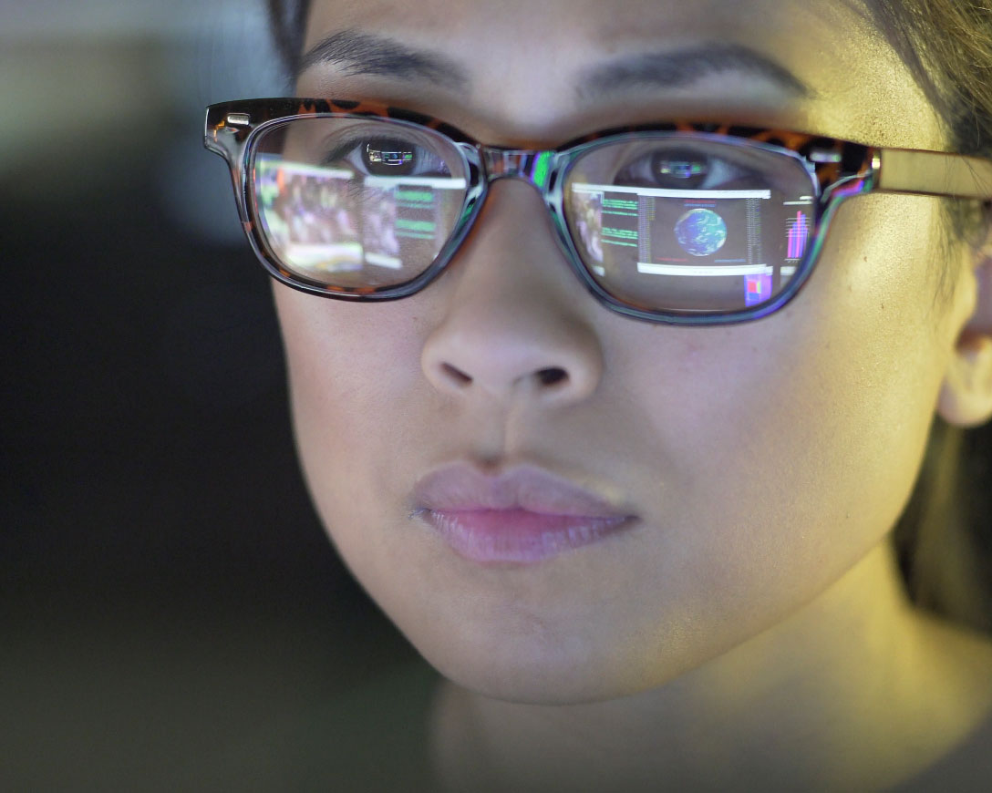 A woman wearing glasses attentively observing a computer screen
