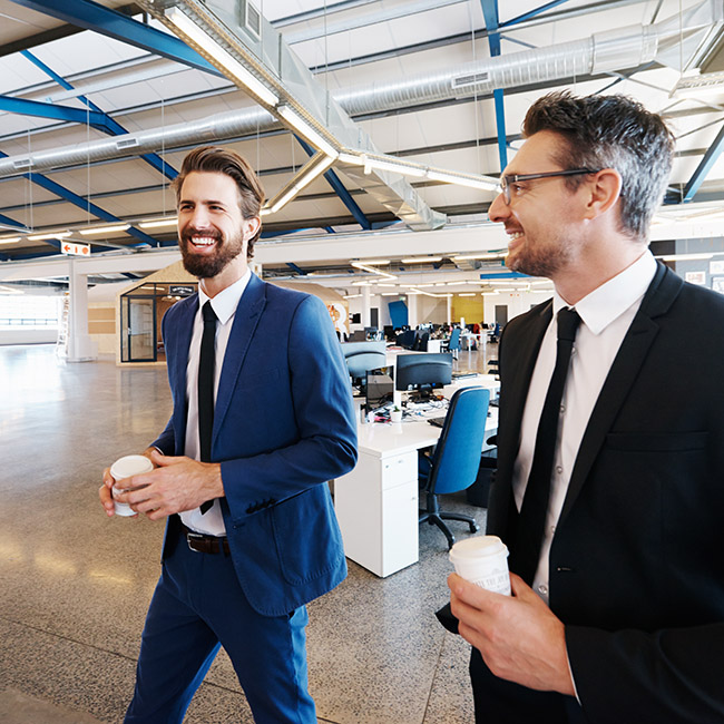 Two businessmen in professional attire walk together through an open office environment
