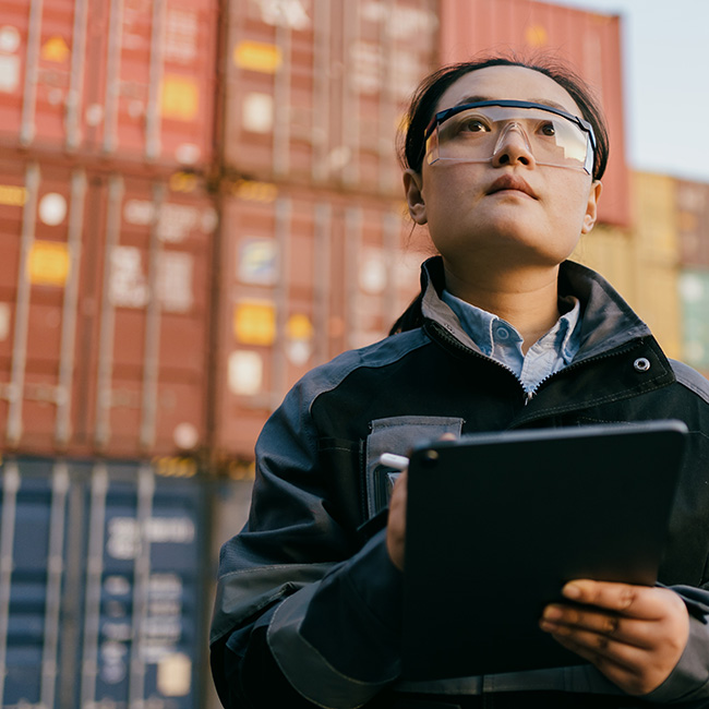 Woman checking shipment status on a tablet with cargo containers in background