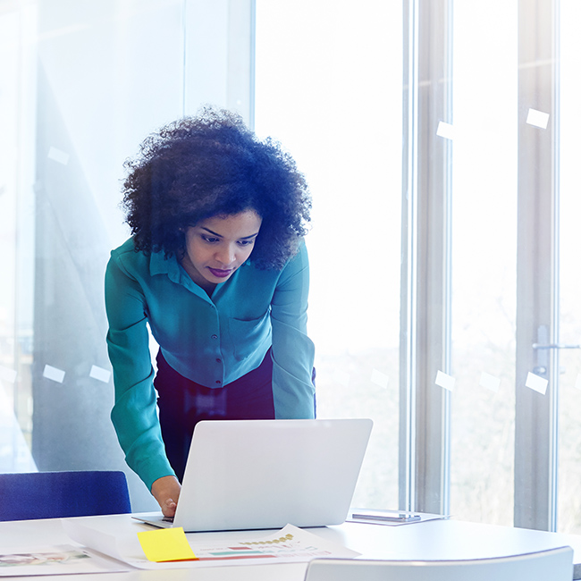 Woman using laptop computer near a window in a bright workspace