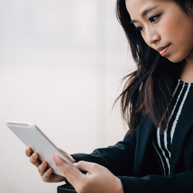 A professional woman in a business suit confidently operates a tablet device, efficiently managing tasks and staying connected.