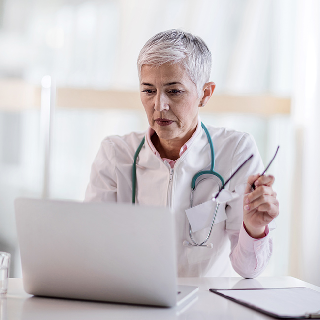 Female medical professional holding a pair of eyeglasses and working on a laptop