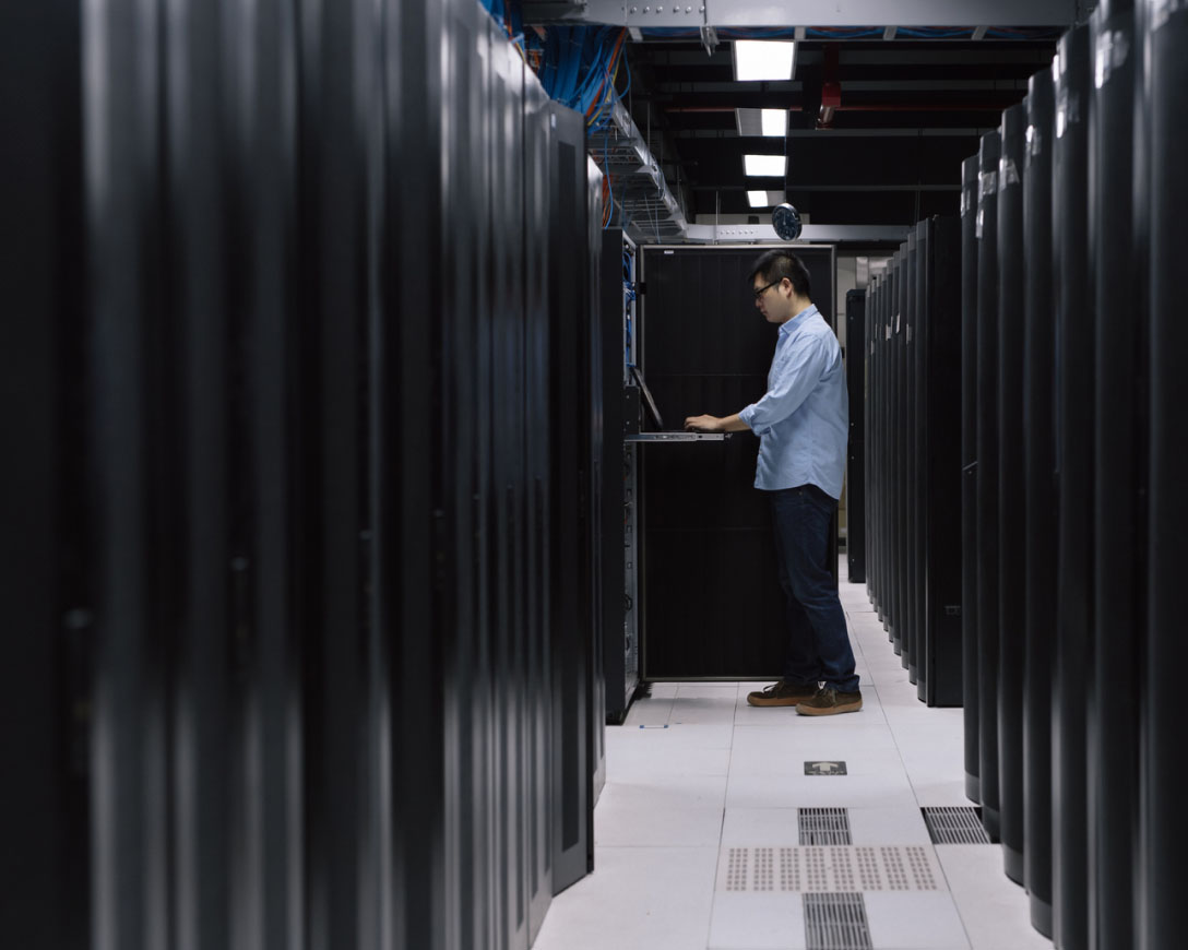 A man working on a laptop in a server room.