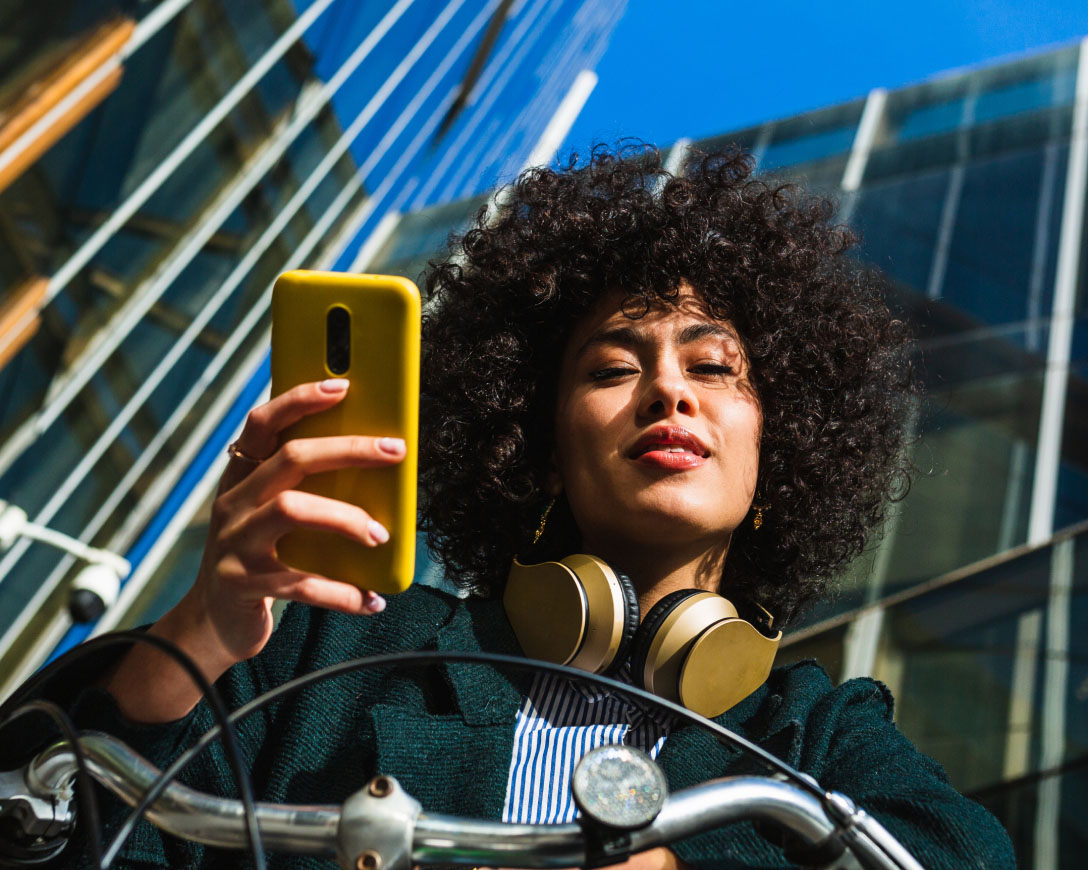 A woman with curly hair wearing headphones while using her phone to listen to music.