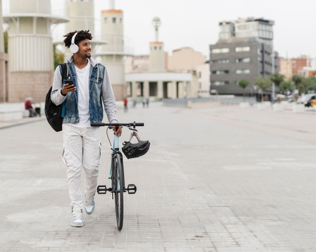 A cyclist wearing headphones strolls along the street, enjoying music while walking with his bike.