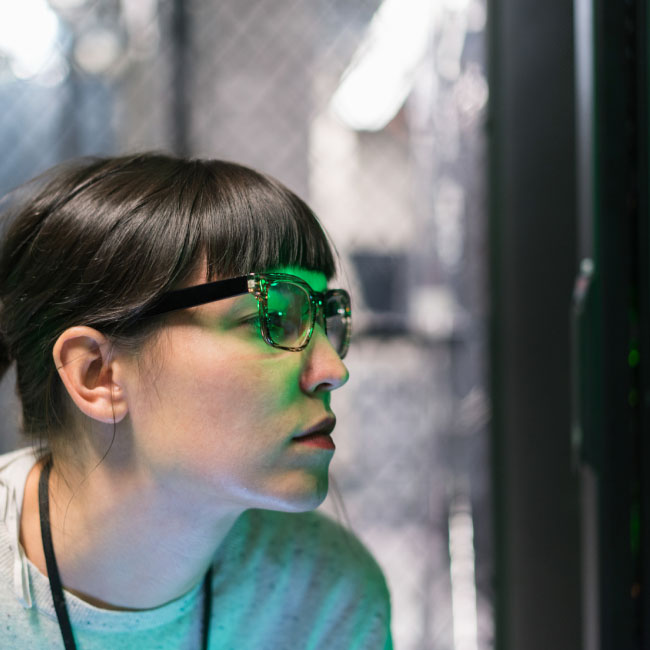 A woman with glasses focused on a computer screen, engrossed in her work.