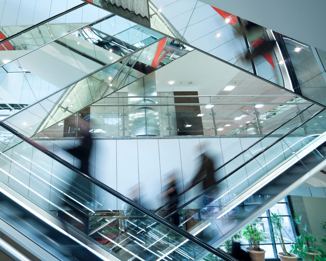 A group of individuals descending on an escalator, moving in unison towards the lower level.