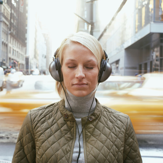 A woman wearing headphones, immersed in music, walks through the bustling streets of a vibrant city.