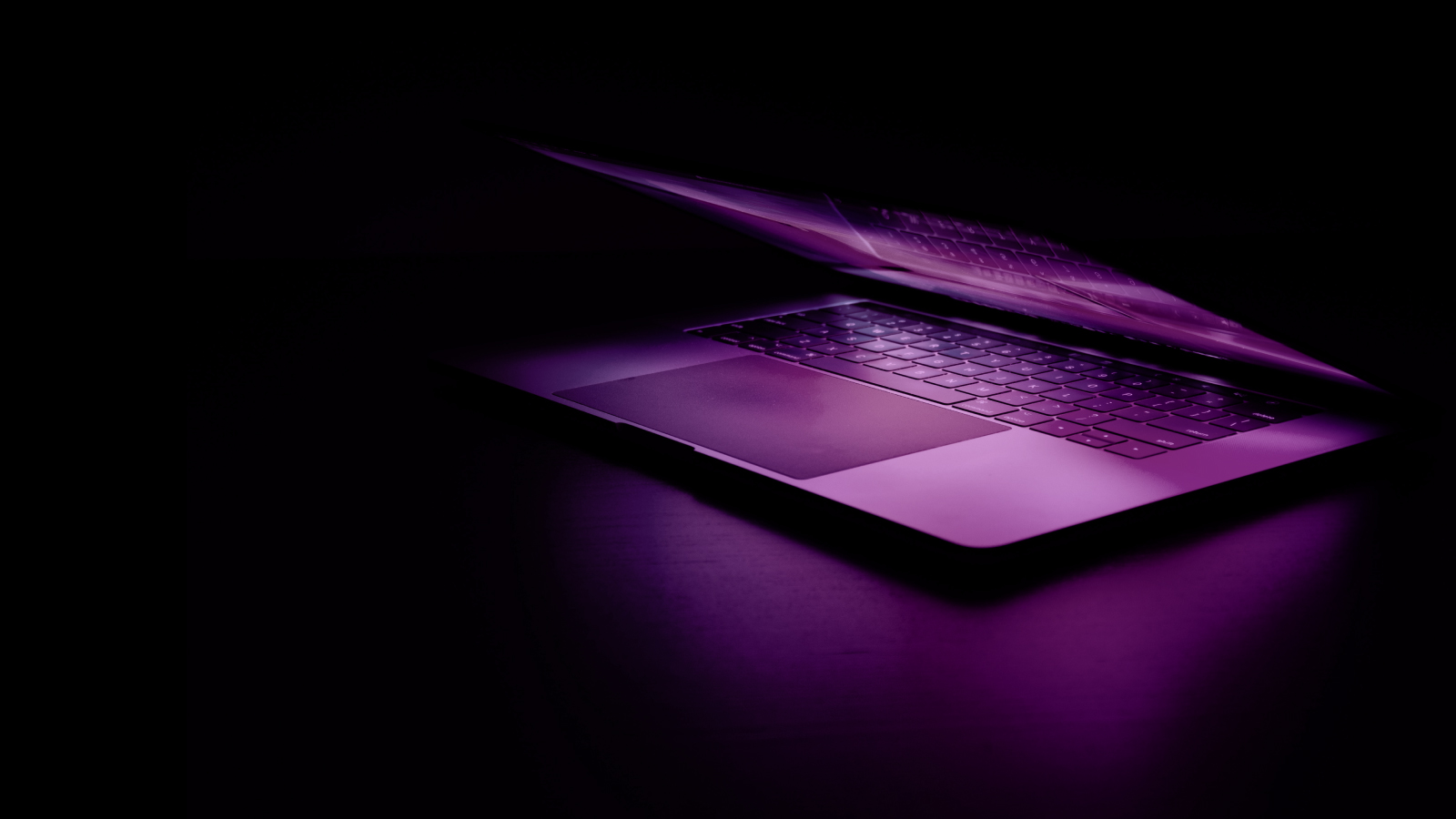 A brightly illuminated purple laptop shines in the darkness, showcasing its vibrant hue and sleek design.