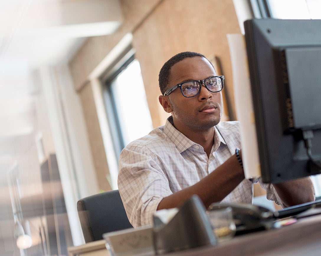 Performance - A man seated at a desk focuses on his monitor