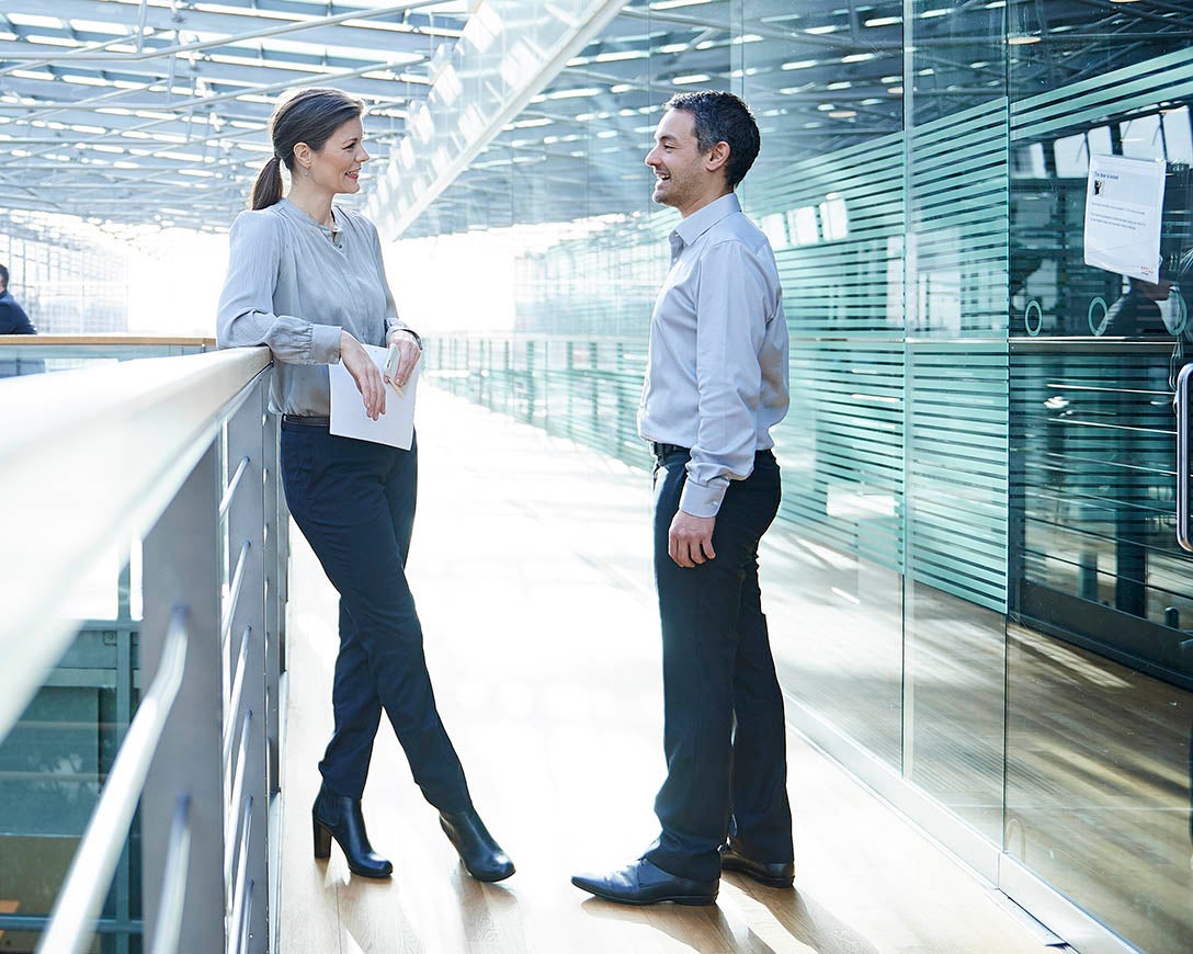 Leadership - Two C-suite colleagues have a conversation in the hallway balcony of a modern office building